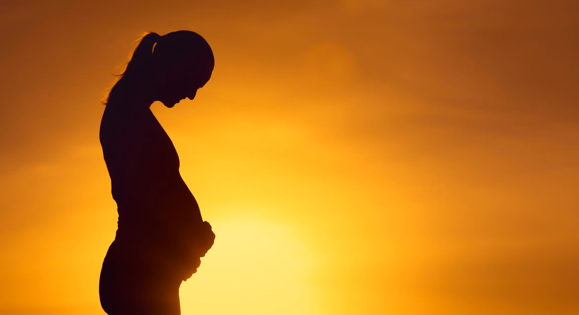 Silhouette of a woman holding her pregnant belly at sunset  